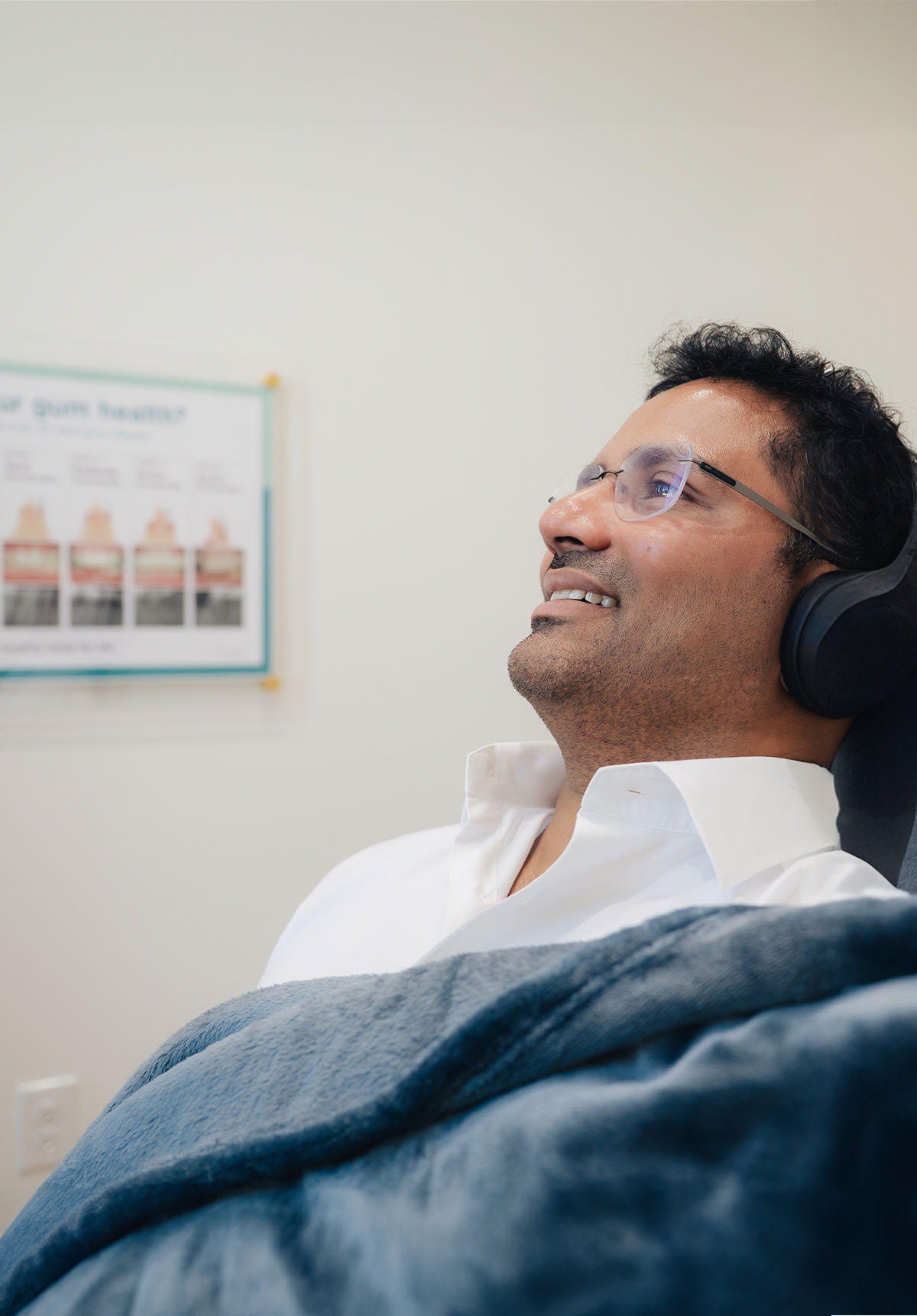 A dental patient reclining in the dental chair with headphones and a blanket